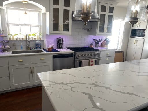 Remodeled white kitchen with marble-look island, gas range and pendant lights